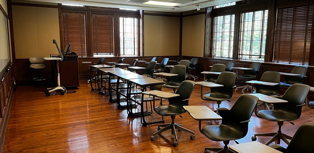 Ayres 111. Room includes singular desks arranged in rows and node chairs that can be moved into different configurations. Instructor podium includes the control panel, instructor screen, and a spot for laptop. Next to the podium is a table that includes the document camera. The document camera table can be raised and lowered by pressing a button on the front of the table.