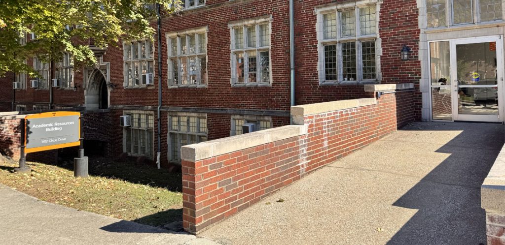 Brick building with sign out front saying Academic Resources building. Has a walkway that is like a bridge leading to entry door.