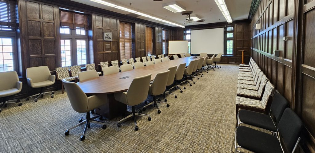 Austin Peay 411. Room includes a conference room table with chairs surrounding it and a screen in the background where the instructor sits
