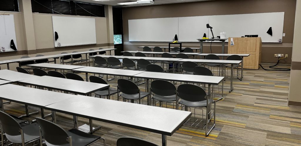 Biosystems Engineering 268. Room includes long tables with chairs arranged around them. Instructor podium includes the control panel, instructor screen, and a spot for laptop. Next to the podium is a table that includes the document camera. The document camera table can be raised and lowered by pressing a button on the front of the table.