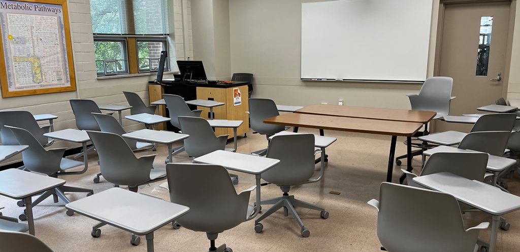 Food Safety and Processing 126. Room includes node chairs that can be moved into different configurations. Instructor podium includes the control panel, instructor screen, and a spot for laptop. Next to the podium is a table that includes the document camera.