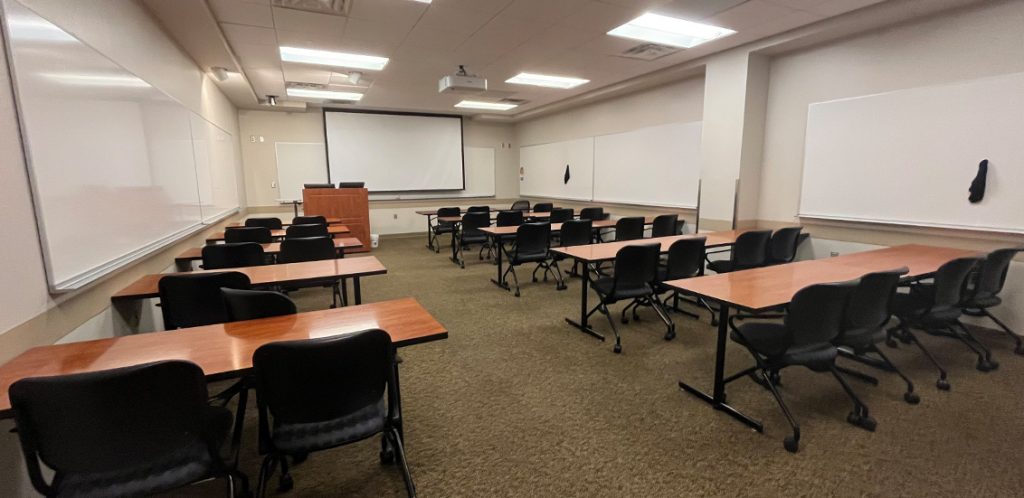 Haslam Business Building 121. Room includes amphitheater style seating. Instructor podium includes the control panel, instructor screen, and a spot for laptop. Next to the podium is a table that is positioned under the ceiling-mounted document camera.