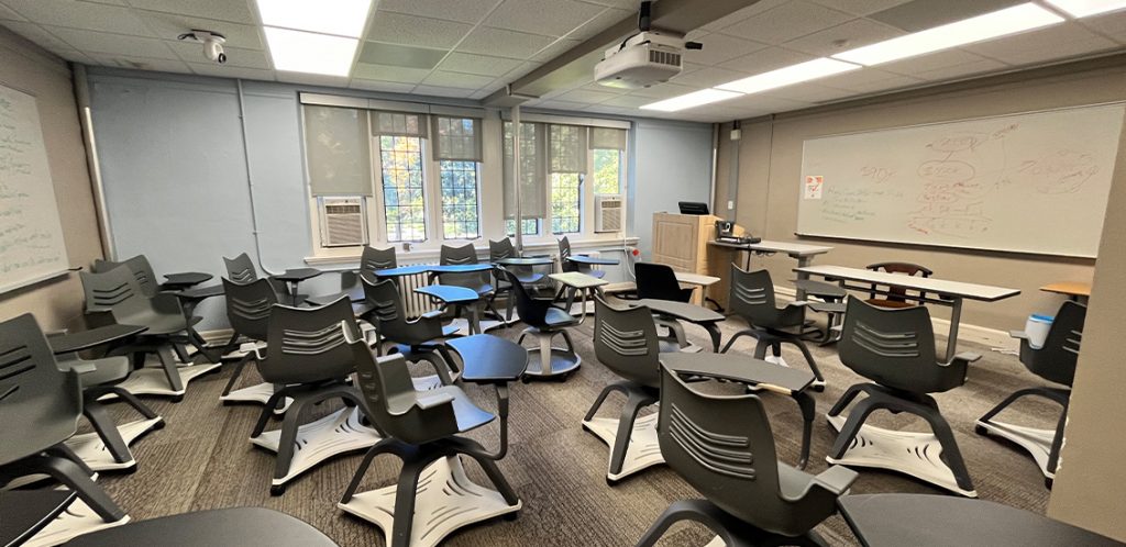 Henson 318. Room includes node chairs that can be moved into different configurations. Instructor podium includes the control panel, instructor screen, and a spot for laptop. Next to the podium is a table that includes the document camera. The document camera table can be raised and lowered by pressing a button on the front of the table.