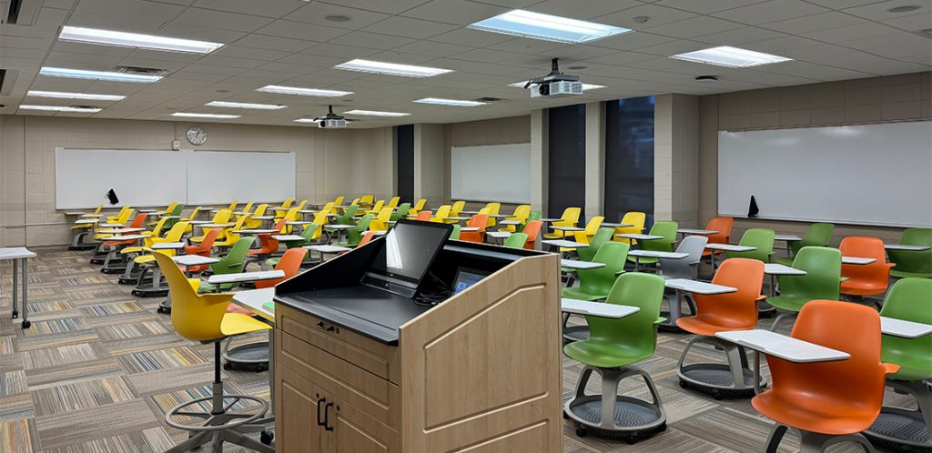 Humanities 51. Room includes node chairs that can be moved into different configurations. Instructor podium includes the control panel, instructor screen, and a spot for laptop. Next to the podium is a table that includes the document camera. The document camera table can be raised and lowered by pressing a button on the front of the table.