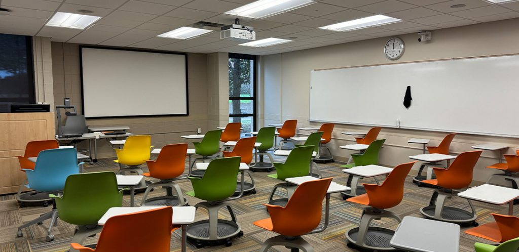 Humanities 58. Room includes node chairs that can be moved into different configurations. Instructor podium includes the control panel, instructor screen, and a spot for laptop. Next to the podium is a table that includes the document camera. The document camera table can be raised and lowered by pressing a button on the front of the table.