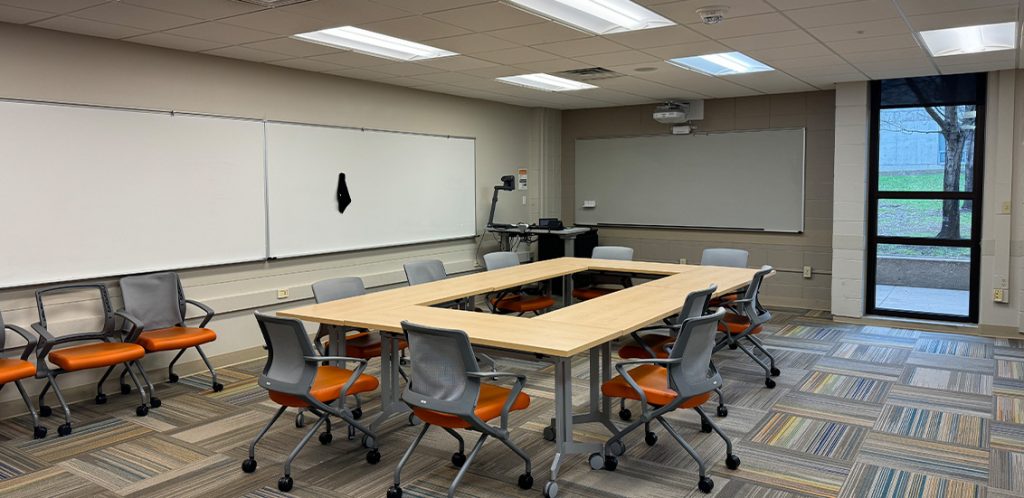 Humanities 62. Room includes tables and chairs that can be moved into different configurations. Instructor podium includes the control panel, instructor screen, and a spot for laptop. Next to the podium is a table that includes the document camera. The document camera table can be raised and lowered by pressing a button on the front of the table.