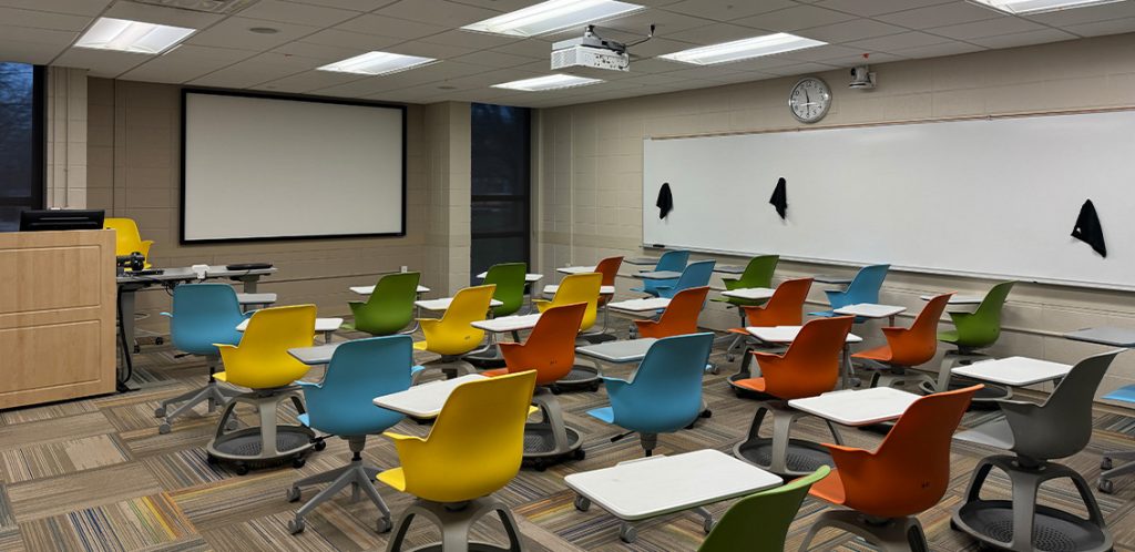 Humanities 68. Room includes node chairs that can be moved into different configurations. Instructor podium includes the control panel, instructor screen, and a spot for laptop. Next to the podium is a table that includes the document camera. The document camera table can be raised and lowered by pressing a button on the front of the table.