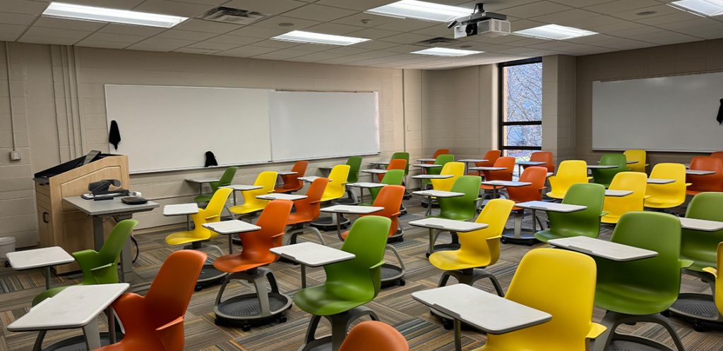 Humanities 111. Room includes node chairs that can be moved into different configurations. Instructor podium includes the control panel, instructor screen, and a spot for laptop. Next to the podium is a table that includes the document camera. The document camera table can be raised and lowered by pressing a button on the front of the table.