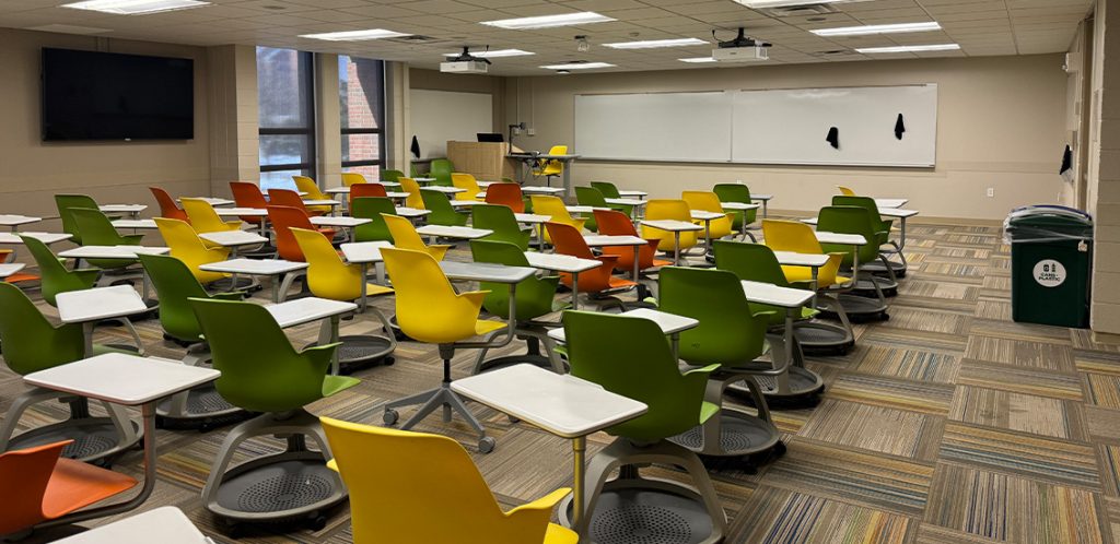 Humanities 206. Room includes node chairs that can be moved into different configurations. Instructor podium includes the control panel, instructor screen, and a spot for laptop. Next to the podium is a table that includes the document camera. The document camera table can be raised and lowered by pressing a button on the front of the table.
