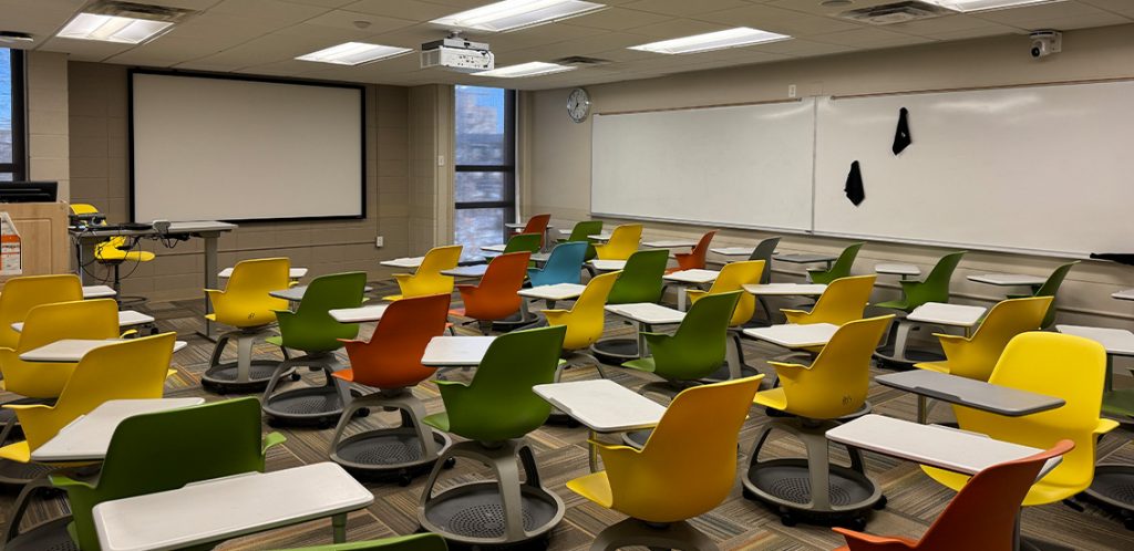 Humanities 219. Room includes node chairs that can be moved into different configurations. Instructor podium includes the control panel, instructor screen, and a spot for laptop. Next to the podium is a table that includes the document camera. The document camera table can be raised and lowered by pressing a button on the front of the table.