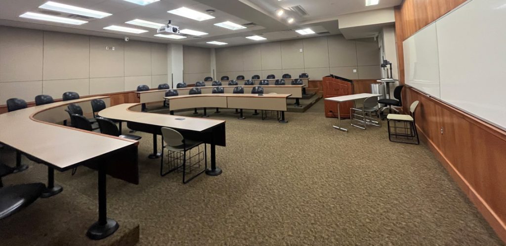 Haslam Business Building 113. Room includes amphitheater style seating. Instructor podium includes the control panel, instructor screen, and a spot for laptop. Next to the podium is a table that is positioned under the ceiling-mounted document camera.
