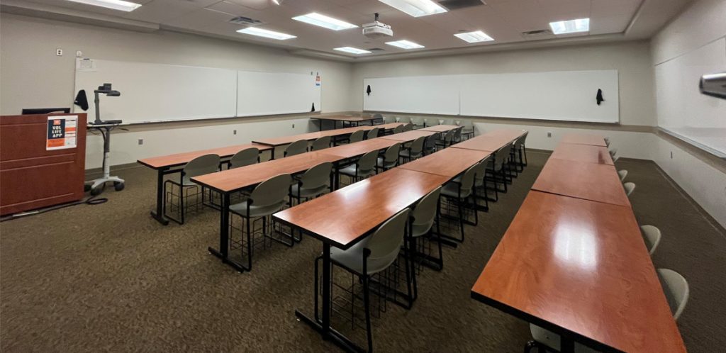Haslam Business Building 130. Room includes tables and chairs. Instructor podium includes the control panel, instructor screen, and a spot for laptop. Next to the podium is a table that is positioned under the ceiling-mounted document camera.