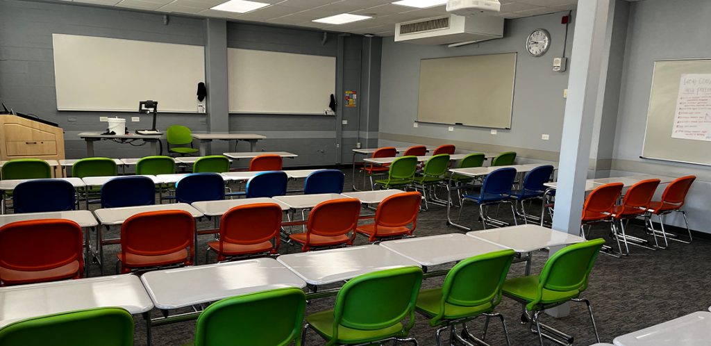 Jessie Harris 413. Room includes individual desks and chairs that can be moved into different configurations. Instructor podium includes the control panel, instructor screen, and a spot for laptop. Next to the podium is a table that includes the document camera. The document camera table can be raised and lowered by pressing a button on the front of the table.